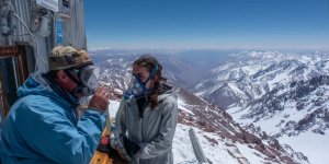 Traveler experiencing symptoms of altitude sickness with oxygen mask at high altitude medical station with snow-capped Andes mountains in background