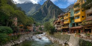 Comprehensive travel guide showing Aguas Calientes town with colorful buildings, thermal baths, restaurants, and Machu Picchu mountain backdrop
