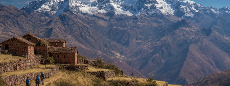 Hikers overlooking the terraces and stone buildings of Huchuy Qosqo with snow-capped peaks behind