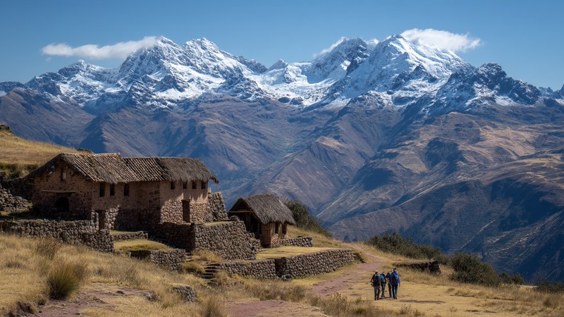 Hikers overlooking the terraces and stone buildings of Huchuy Qosqo with snow-capped peaks behind