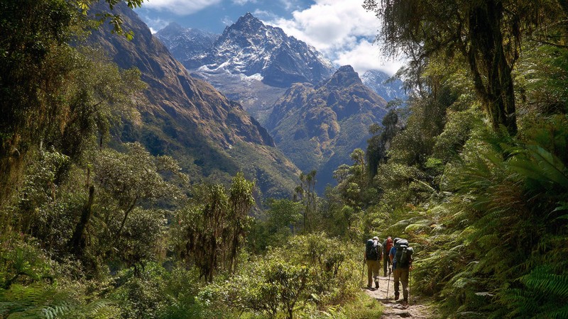 Adventure travelers navigating jungle terrain with mountain backdrop on the Inca Jungle Trek route