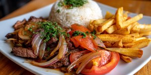 Plate of lomo saltado with beef, onions, tomatoes, fries and rice