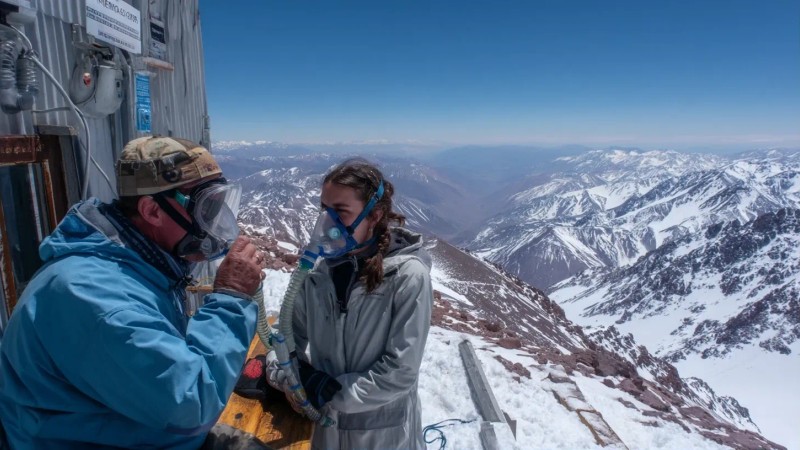 Traveler experiencing symptoms of altitude sickness with oxygen mask at high altitude medical station with snow-capped Andes mountains in background