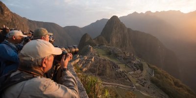 Photography enthusiasts capturing golden hour light at Machu Picchu with professional cameras, using wide-angle lenses to frame ancient terraces against dramatic mountain backdrops, and waiting for perfect sunrise conditions
