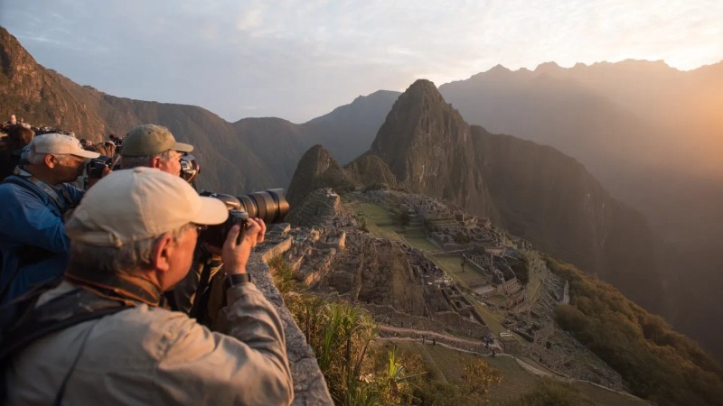 Photography enthusiasts capturing golden hour light at Machu Picchu with professional cameras, using wide-angle lenses to frame ancient terraces against dramatic mountain backdrops, and waiting for perfect sunrise conditions