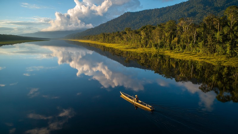 Canoe gliding on a mirror‑calm oxbow lake in Manu National Park at sunrise