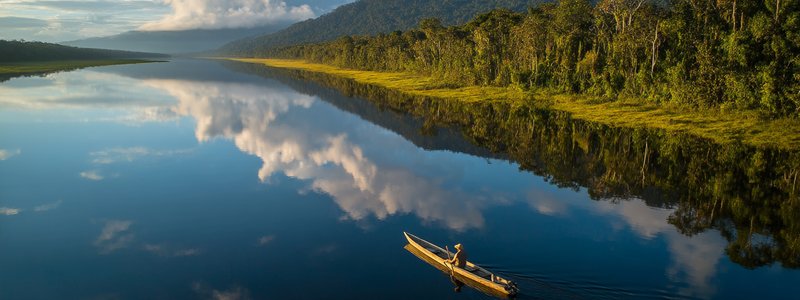 Canoe gliding on a mirror‑calm oxbow lake in Manu National Park at sunrise