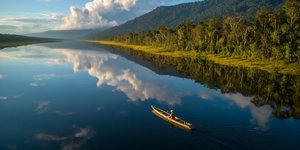 Canoe gliding on a mirror‑calm oxbow lake in Manu National Park at sunrise
