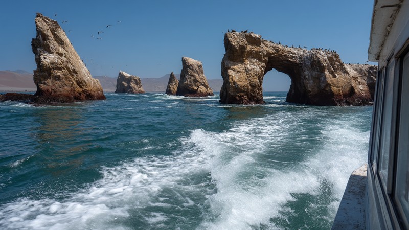 Boat approaching the Ballestas Islands with sea lions and arches visible in Paracas, Peru