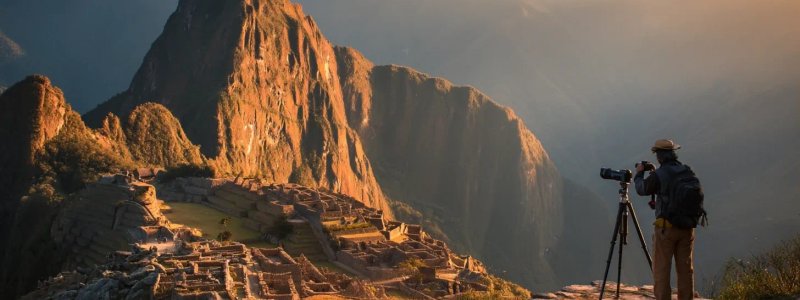 Professional photographer capturing Machu Picchu sunrise with telephoto lens on sturdy tripod as golden light illuminates ancient terraces