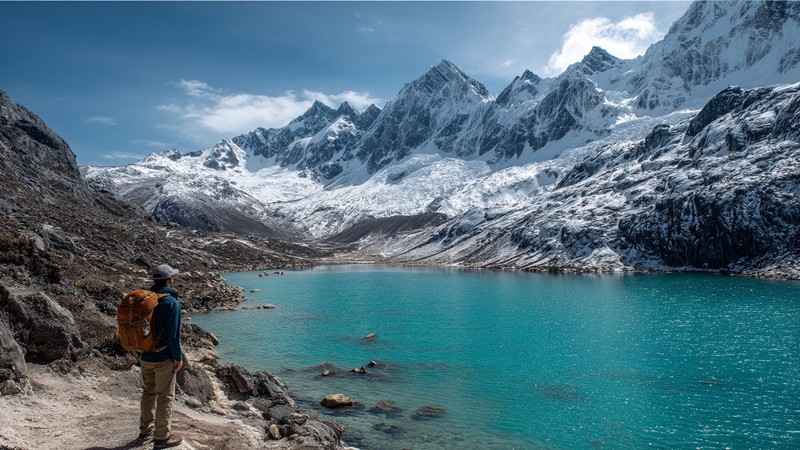 Trekker looking at a turquoise lake and snow-capped peaks on the Santa Cruz Trek
