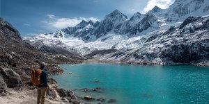 Trekker looking at a turquoise lake and snow-capped peaks on the Santa Cruz Trek