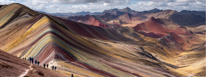 Rainbow Mountain’s colorful striped slopes with hikers in the foreground