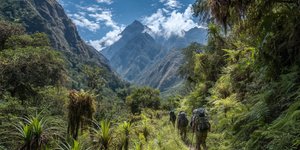 Adventure travelers navigating jungle terrain with mountain backdrop on the Inca Jungle Trek route