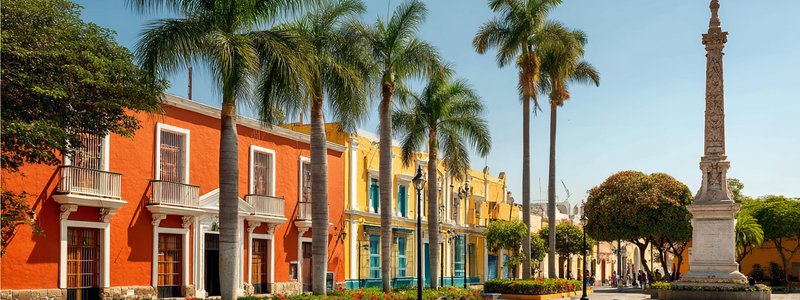 Colourful colonial buildings around Trujillo’s Plaza de Armas with palm trees and the Liberty Monument